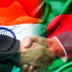 "India and Bangladesh flags merged in the background as two individuals shake hands in the foreground, symbolizing diplomatic relations."
